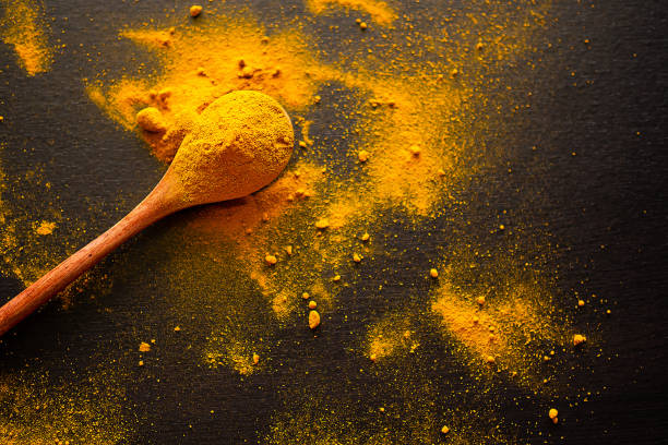 istock Turmeric powder on wooden spoon with black background. 1298762519