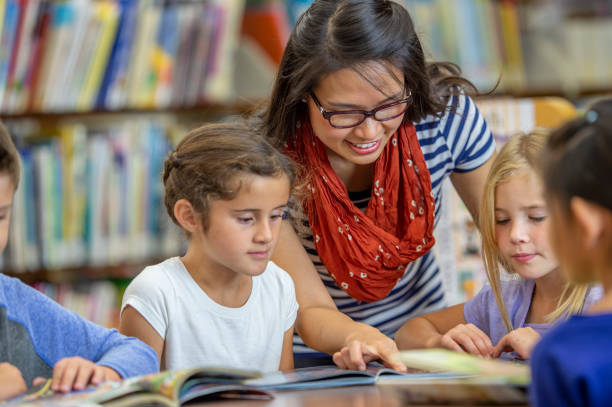 istock Asian teacher helping students to read 1298780513