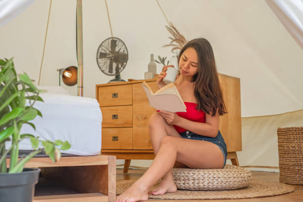 Indonesia mid adult woman reading a book in the cozy room Front view shot of Indonesia mid adult woman reading a book in the cozy room, sitting on the floor with a cup of coffee on her hand staycation hotel asian stock pictures, royalty-free photos & images