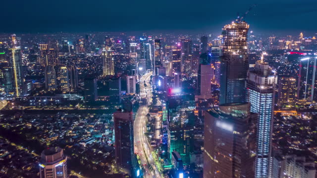 Stunning City View of Futuristic Skyline at Night, Skyscrapers in Asian Indonesian Capital Jakarta with flashing lights and Car Traffic Flow on Main road, Aerial Hyperlapse Time Lapse, Drone View