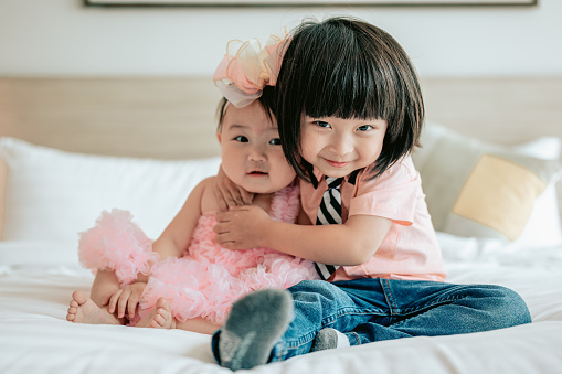 Portrait of happy kids playing in white bedroom. Little boy and girl, brother hugging little sister on the bed.Happy family lifestyle concept.