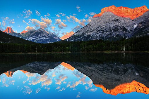 Golden sunrise reflecting off the calm waters of Wedge Pond beneath Mount Kidd in the Kananaskis Country of the Canadian Rockies near Banff National Park, Alberta, Canada.