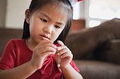 アジアの子供の女の子の手を閉じるは、家の中で意図と楽しみを持つ文字列にビーズを通しています。