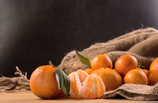 Fresh juicy tangerines or mandarins with green leaves on sack cloth and wooden table. winter seasonal fruits