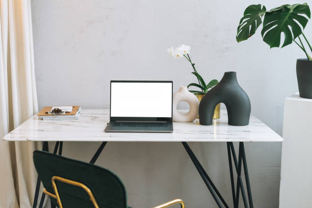 istock Modern workplace with an open laptop with white screen and green monstera on marble table, mock up, template 1298817388