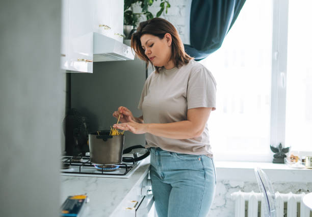 Beautiful brunette young woman plus size body positive cooking pasta in kitchen at home Beautiful brunette young woman plus size body positive cooking in kitchen at home large pasta pot stock pictures, royalty-free photos & images