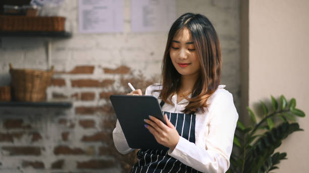 istock Smiling coffee shop owner standing inside her shop and using digital tablet receive orders from customers. 1298822978