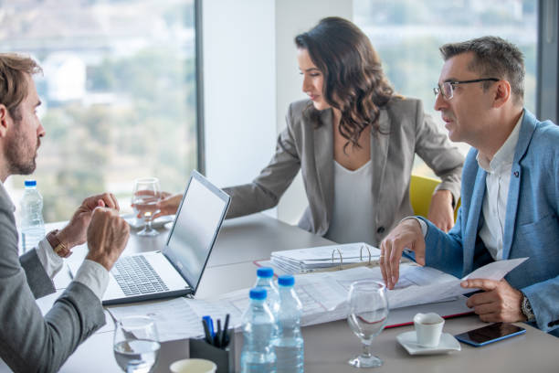 istock Businessman holding sheet at the conference table and pointing at issues 1298824030