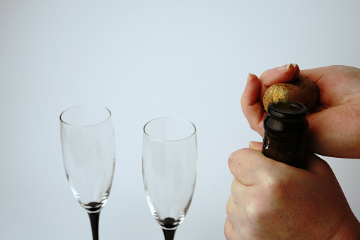 We open a bottle of champagne on a white background with glasses. Hands and a traffic jam are visible. Close