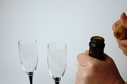We open a bottle of champagne on a white background with glasses. Hands and a traffic jam are visible. Close