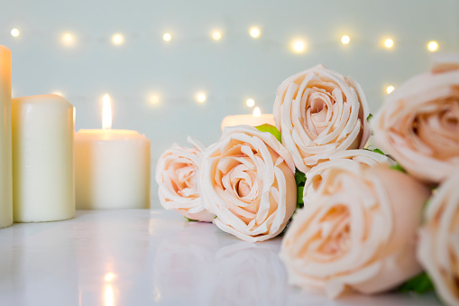 Beige rose bouquet and white candles against bokeh lights background for clean valentine, wedding theme.