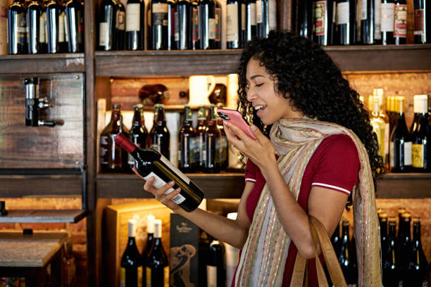 istock Hispanic Woman Conversing on Phone While Shopping for Wine 1298830854