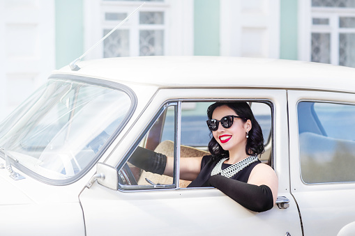 young woman in black sunglasses driving a retro car, sunny summer day