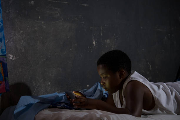 African boy working on his tablet in the dark on his bed
