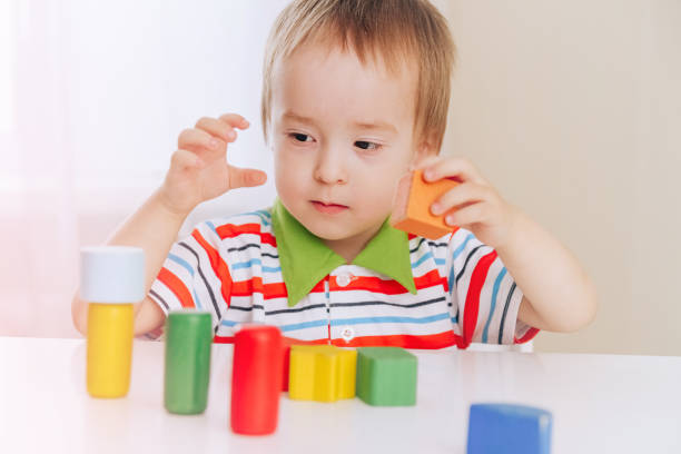 istock a small Caucasian boy sits at a white table and plays with bright colored wooden figures, a concept of early development and education 1298834312
