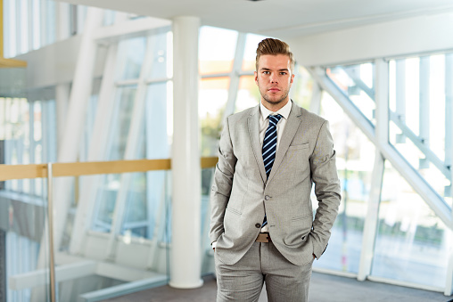 Young businessman standing in a hallway with hands in his pockets and looking at camera.