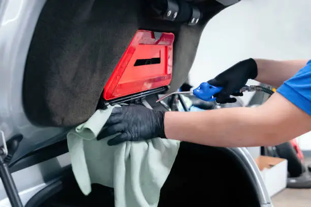 Close up of car wash worker wearing protective gloves and cleaning car trunk with compressed air and a wipe