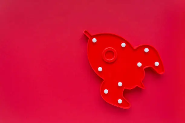 Red rocket ship lamp on red background. Cosmonautics Day concept. Top view, copy space