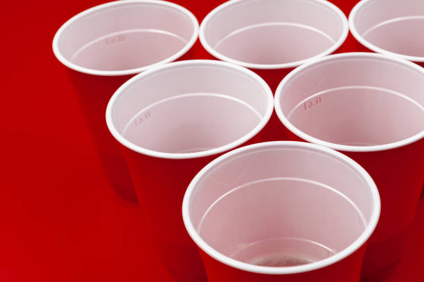 istock Cups and plastic ball on red background. Beer pong game 1298843906