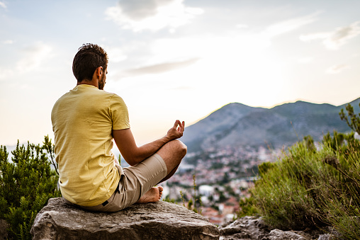 Young man preforms yoga in mountains at sunset.
