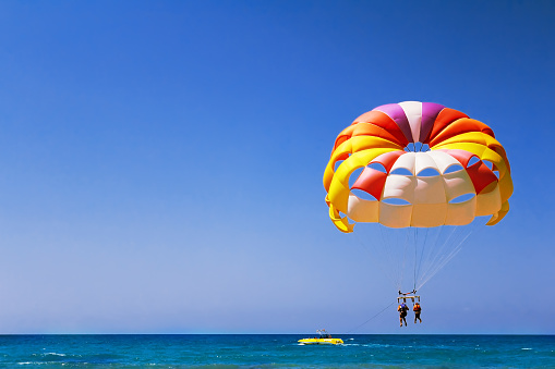 A large parachute with two girls flies in the air over the sea.