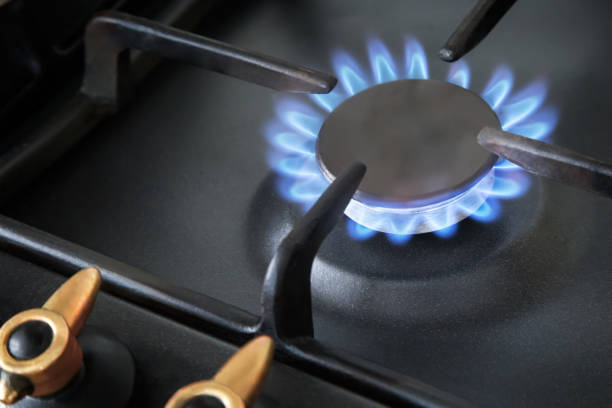 A fragment of a gas stove with a lit burner. Gas stove with included burner, blue flame natural gas burning. gas stove burner stock pictures, royalty-free photos & images