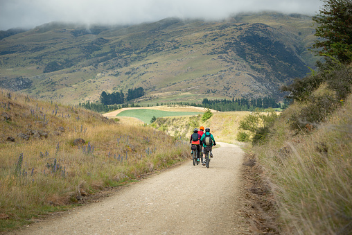 Three people cycling the Otago Central Rail Trail among mountain ranges between Waipiata and Middlemarch, South Island, New Zealand