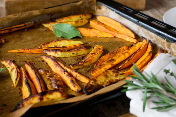 fresh oven baked sweet potato fries with italian herbs and olive oil served on a baking tray at home