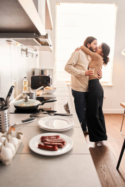 istock Couple embracing while standing in kitchen at home together 1298854682