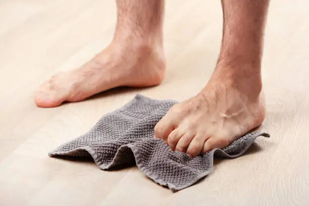Photo of man doing flatfoot correction gymnastic exercise grabbing towel at home