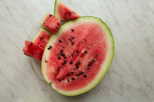 istock Ripe watermelon cut into slices on a light table by window, still life. top view 1298859059