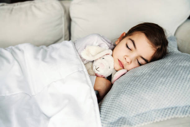 istock Ill little girl lying on sofa at home, hugging her bunny and sleeping. 1298860758