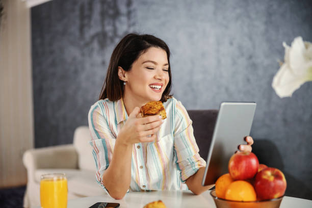 istock Happy woman sitting at dining table, having healthy breakfast and using tablet. Woman using tablet for hanging on social media. 1298861553