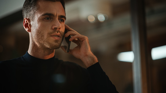 Handsome Caucasian Male is Making a Phone Call while Standing in Meeting Room Behind Glass Walls in an Creative Agency. Project Manager Talking About Business Strategy on Smartphone.