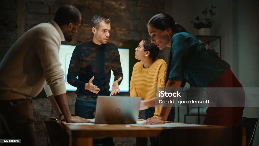 Diverse Multiethnic Team are Having a Conversation in a Meeting Room Behind Glass Walls in a Creative Office. Colleagues Lean On a Conference Table and Discuss Business, App User Interface and Design. Marketing Stock Photo