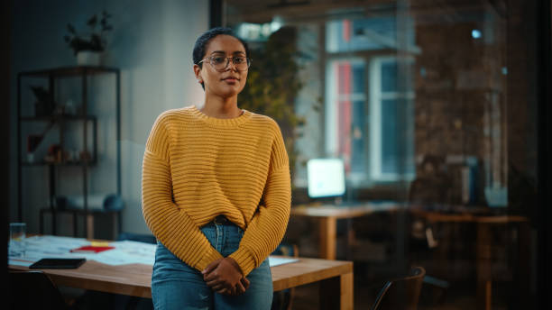 Portrait of a Young Latina with Short Dark Hair and Glasses Posing for Camera in Creative Office Environment. Beautiful Diverse Multiethnic Hispanic Female Wearing Yellow Jumper is Happy and Smiling. Portrait of a Young Latina with Short Dark Hair and Glasses Posing for Camera in Creative Office Environment. Beautiful Diverse Multiethnic Hispanic Female Wearing Yellow Jumper is Happy and Smiling. non binary gender stock pictures, royalty-free photos & images