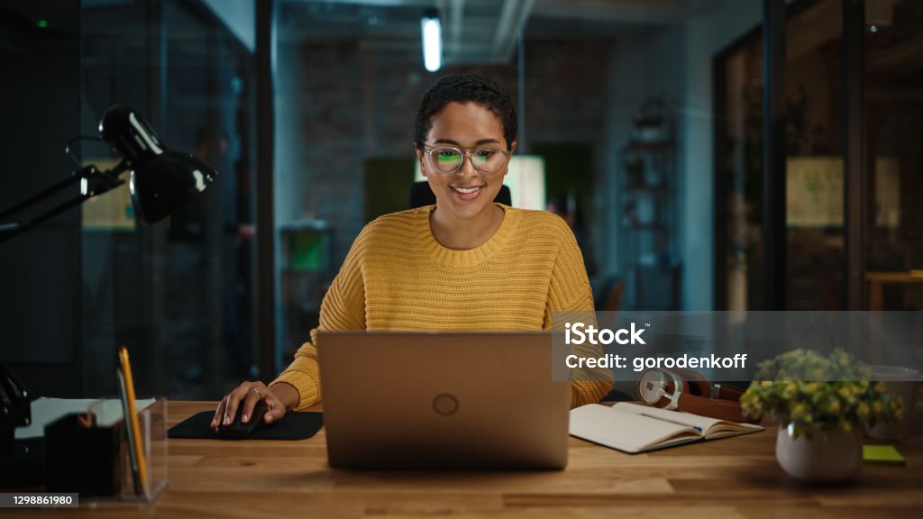 Portrait of Young Latina Marketing Specialist Working on Laptop Computer in Busy Creative Office Environment. Beautiful Diverse Multiethnic Female Project Manager is Browsing Internet. Women Stock Photo