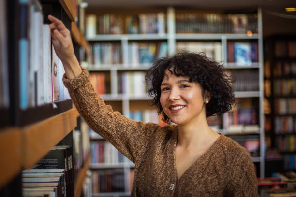 istock Smiling girl in the library chooses a book. 1298862123