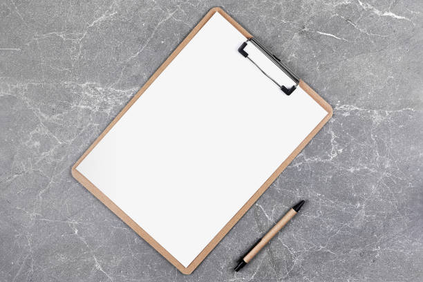 istock Blank clipboard with white sheet and pen on gray marble background. A4 holder. Empty document holder with place for text. Office stationery. 1298862136