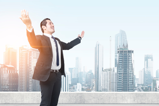 Asian businessman standing with raised hand on the rooftop with skyscrapers background