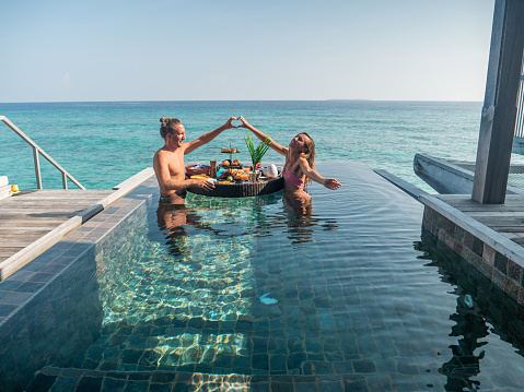 Couple enjoying tropical vacations from an infinity pool in private over water villa. People travel luxury holidays