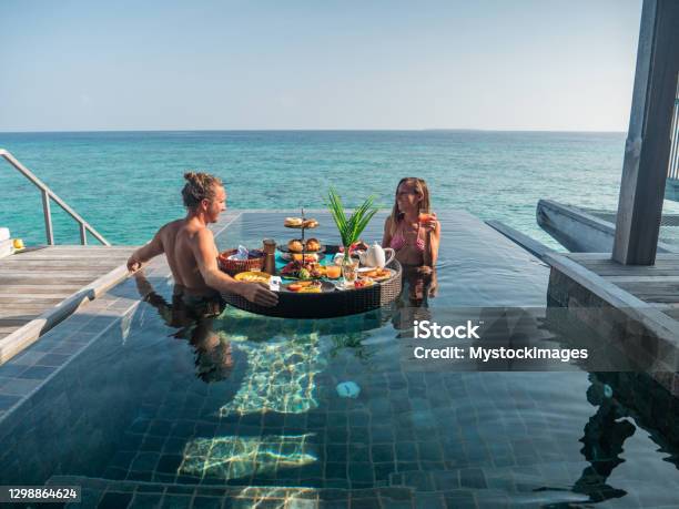 Couple Enjoying Floating Breakfast In Private Overwater Bungalow Stock Photo - Download Image Now