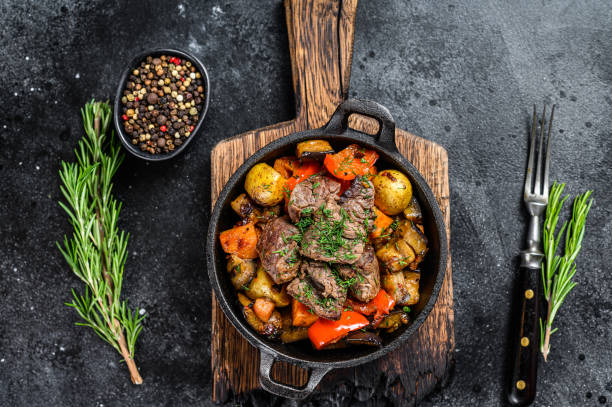 istock Meat stew in cooking pot on dark rustic cutting board. Black background. Top view 1298867589