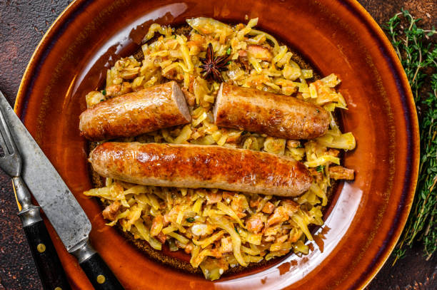 istock Bigos Stewed cabbage with mushrooms and meat sausages on a plate. Dark background. Top view 1298873752