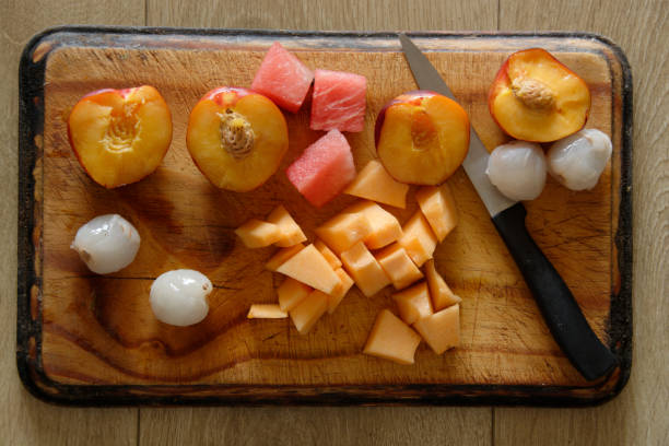 Cut up Fruit on a wooden chopping board with a black handled knife.