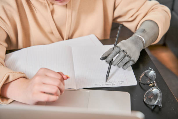 istock Girl with prosthesis arm sitting at table and writing her homework 1298875289
