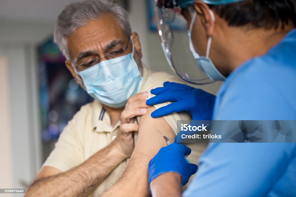Doctor injecting vaccine into arm of senior male patient Vaccination Stock Photo