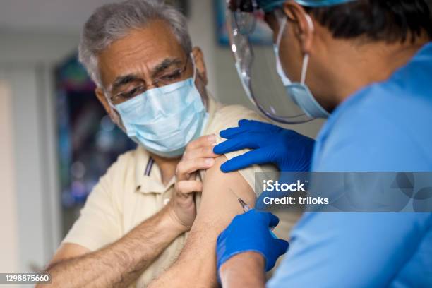 Doctor Injecting Vaccine Into Arm Of Senior Male Patient Stock Photo - Download Image Now