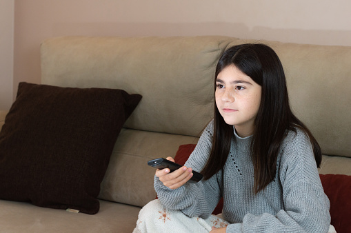 girl on the sofa watching tv with the remote control in hand