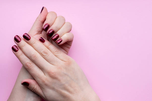 istock Female hands with beautiful manicure - dark red glittered nails on pink background with copy space 1298878192